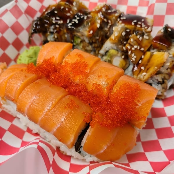 Two sushi rolls in a red and white checkered paper boat, one with salmon and roe, the other with eel.