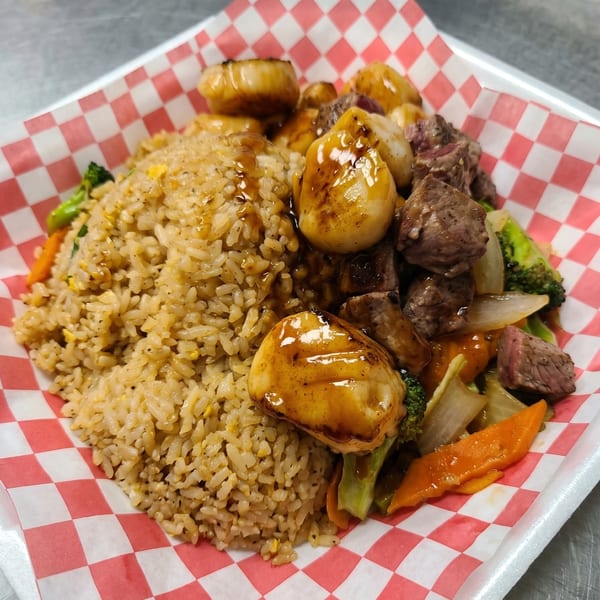 Hibachi steak, scallops, and fried rice with vegetables in a red and white checkered paper-lined container.