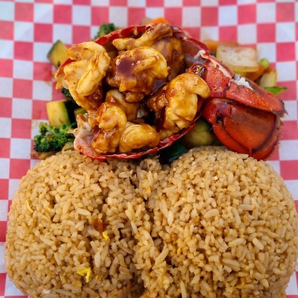 Lobster tail with shrimp, vegetables, and fried rice on a red and white checkered paper.
