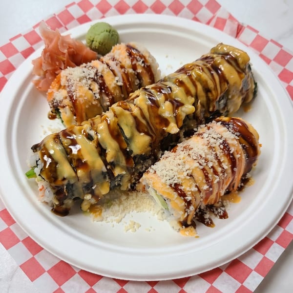 Sushi rolls drizzled with sauce and topped with white crumbles, served with ginger and wasabi.