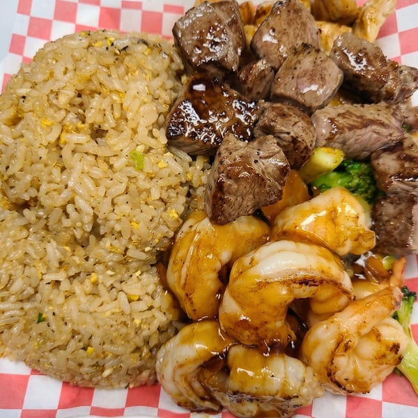 Hibachi steak and shrimp with fried rice and broccoli on a red and white checkered paper.