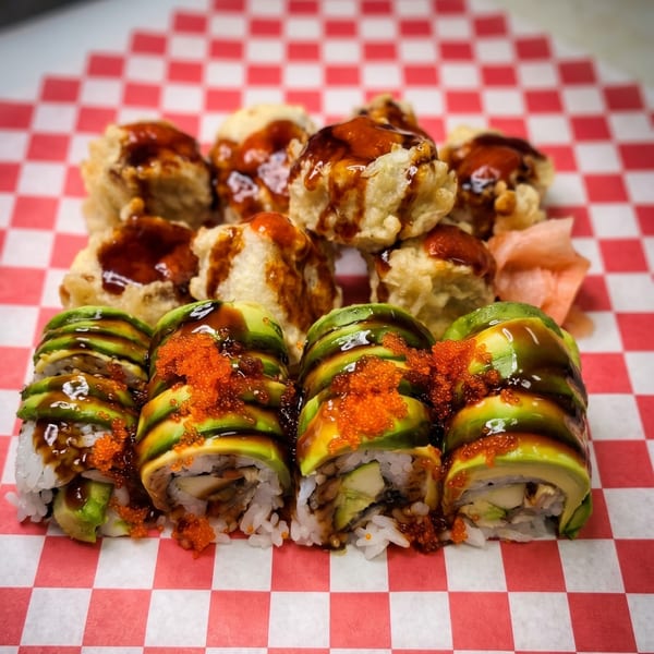 Dragon sushi rolls with avocado, roe, and sauce, alongside fried tempura pieces on checkered paper.